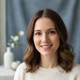 Portrait of a smiling young North American woman with clear skin, looking trustworthy against a soft blue background.