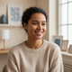 A candid headshot of a smiling young woman, with a relaxed and content expression, against a softly blurred cream and blue ba